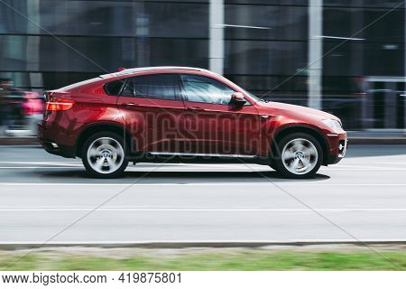 Side View Rolling Shot With Red Car In Motion. Bmw X6 Crossover Driving Along The Street In City Wit
