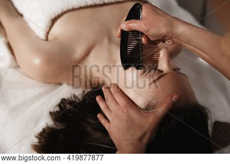 Hands Massaging Young Woman Face With Rade Gua Sha Stones At An Asian Beauty Clinic. Side View. Rela