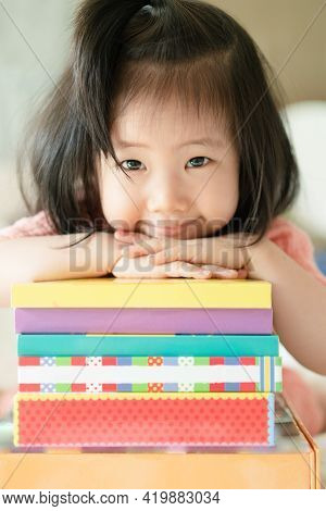 Vertical Image Of Asian Toddler Portrait Put Her Chin And Smiling Over Her Hands On Stack Of Books, 