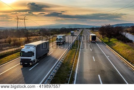 Highway Transit. Convoy Or Caravan Of Transportation Trucks Passing On A Highway At Amazing Sunset. 