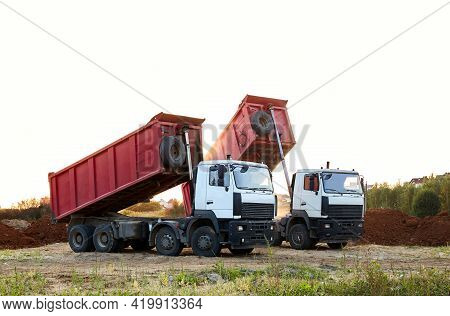 Two Red Dump Trucks Simultaneously Lifted The Bodies To Unload The Sand. Cargo Transportation Servic