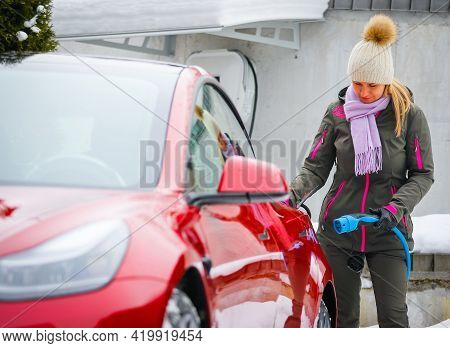 Stylish Girl Stands Near The Electric Car And Waits For The Car To Charge. Connecting The Plug Of Th