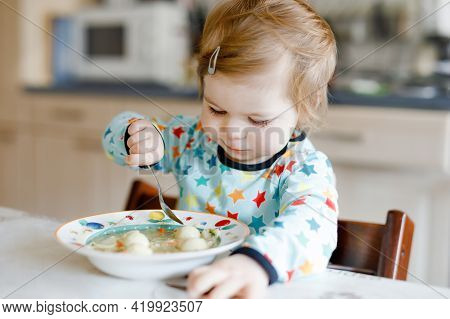 Adorable Baby Girl Eating From Spoon Vegetable Noodle Soup. Food, Child, Feeding And Development Con