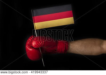 Boxer Hand Holds Flag Of Germany. Boxing Glove With The Germanian Flag. Black Background