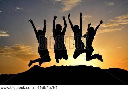 Silhouette Of Happy Group Of Girls Jumping At Sunset. Concept Of Friendship Or Freedom. Unrecognizab