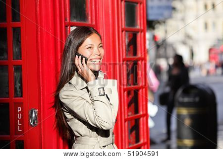London business woman on smart phone by red phone booth. Communication concept with young multiracial Asian businesswoman on smartphone or mobile phone in London, England, United Kingdom.