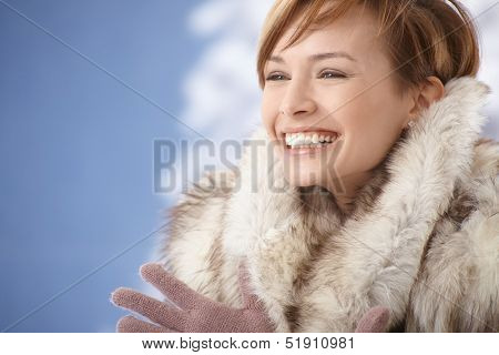 Portrait of happy young woman wearing fur coat, enjoying winter sunshine.