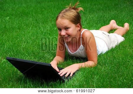Young girl lying on grass in a park with laptop computer