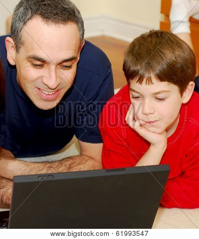 Father and son lying on the floor at home and looking into a portable computer