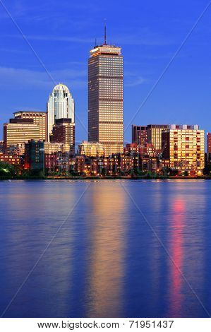 Boston city skyline at dusk with Prudential Tower and urban skyscrapers over Charles River with lights and reflections.