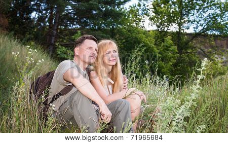 Hiking couple - hikers resting in valey. Young woman and man hiker with backpacks sitting by the for