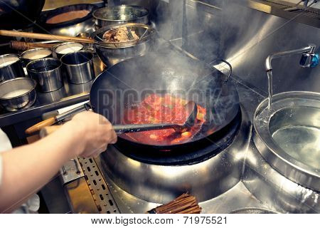 Chef is stirring vegetables with sour sauce in wok at commercial kitchen, toned image