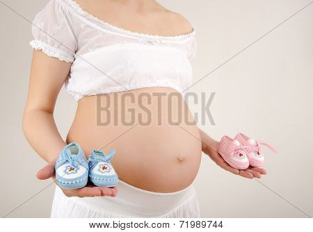 Close up on pregnant belly with pink and blue new born shoes.