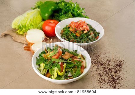 Plates of traditional Arabic salad fattouch and tabbouleh on a rustic background