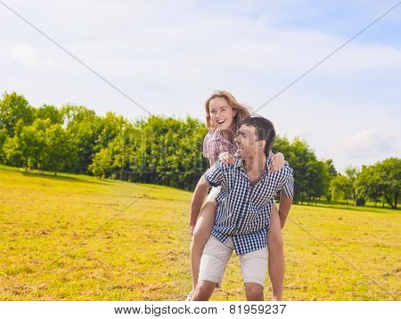 Portrait Of Happy And Cheerful Young Caucasian Couple Piggybacking Outdoors.summer Vacations And You
