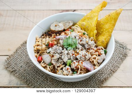 Spicy instant noodle soup with minced pork on wood background.
