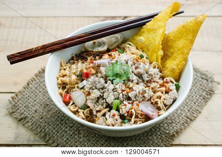Spicy instant noodle soup with minced pork on wood background.