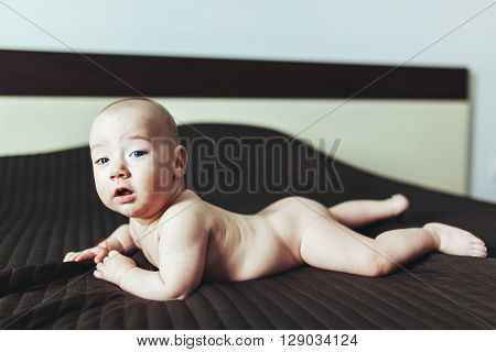 Portrait of a cute naked baby boy toddling on the bed