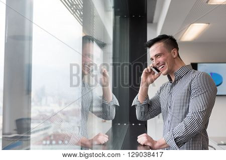 relaxed young businessman speaking on smart phone at modern startup business office meeting room  with big window and city in backgronud