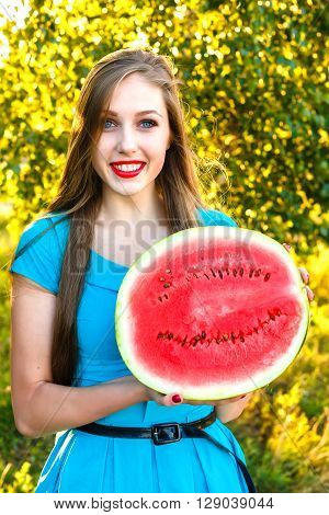 Smiling young blonde woman with long hair holding half of juicy watermelon