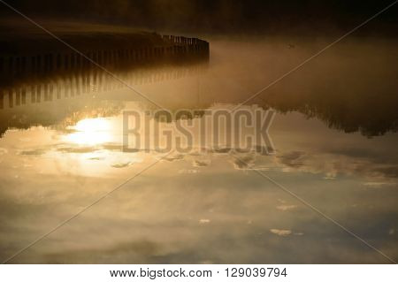 Morning sky and sun water reflection with mist rising from the lake