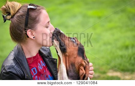 Young woman with an affectionate one year old Basset hound (Canis lupus familiaris) in the yard of a hobby farm.  Girl loves her dog, wet kisses from her one year old Basset hound.