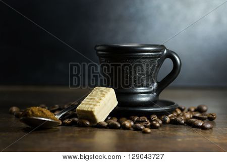 Cup of hot coffee with spoon and candy on wooden background