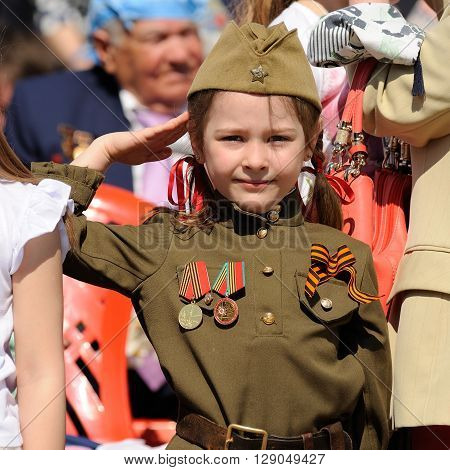 Orel Russia - May 9 2016: Celebration of 71th anniversary of the Victory Day (WWII). Little girl saluting in Russian military uniform with medals and St.George ribbon closeup