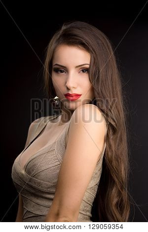 Young brunette woman in evening dress with beautiful make-up posing on black background. Looking at camera