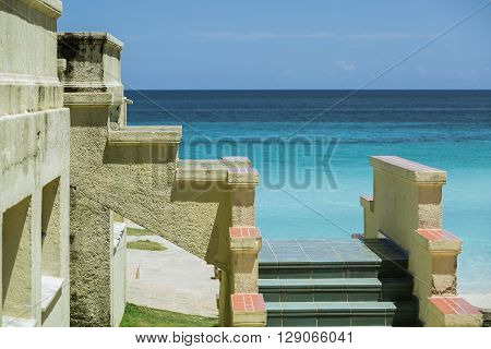 Fragment of an old antique vintage steps attached to the building wall against tranquil azure ocean and blue sky background