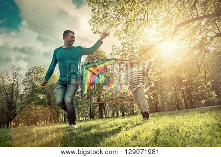 Runnings little boy and father flies with them kite in the park under sunligt.