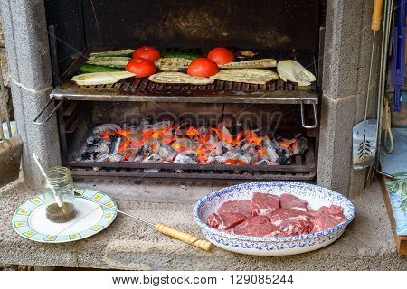 Grilling vegetables on barbecue tomatoes zucchini and eggplants with a dish of beef meat waiting to be cooked