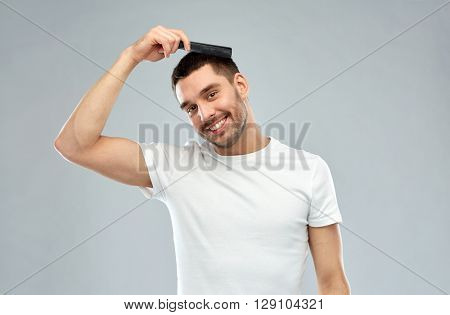 beauty, grooming and people concept - smiling young man brushing hair with comb over gray background
