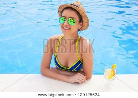 Pretty brunette woman in a hat enjoying lemonade in a swimming pool