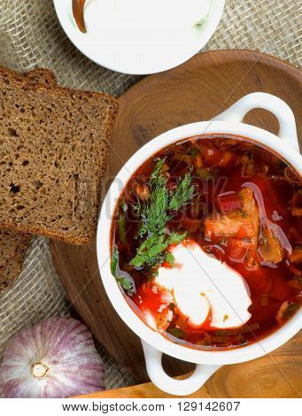 Traditional Soup Borscht with Beet Vegetables and Meat. Top View of Borscht in Bowl closeup on Wooden Plate with Brown Bread Garlic and Sour Cream