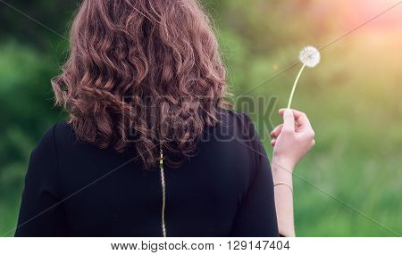 Beautiful girl standing with dandelion in hand