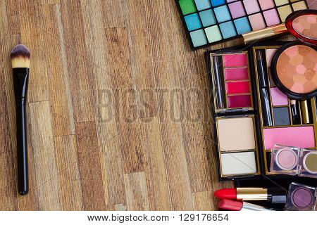 Frame of  brushes, lipsticks, maskara, eye shadows and  powder on wooden table, top view