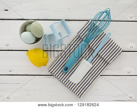 Eggs in a ceramic bowl with a whisk and lemon on a rustic white painted wood table top shot from above