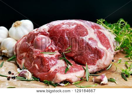 Raw lamb leg on crumpled paper background with herbs.