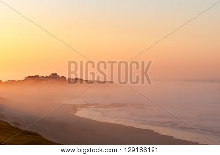 The town of Buffels Bay rising above the mist over sea in the first rays of the rising sun as seen from Buffelskop