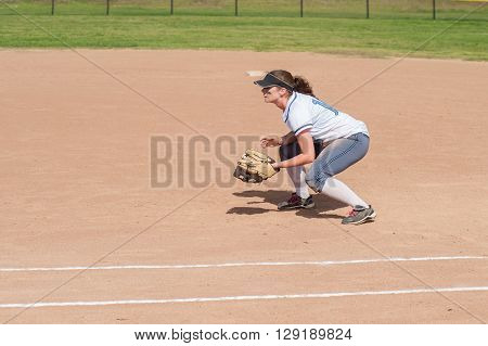 Female softball player crouched and ready for the ball on defense.