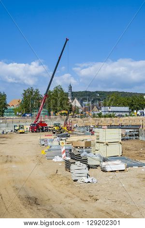Workers Assist The Crane Carrying Building Material To The Construction Site.
