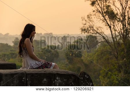 ANGKOR WAT CAMBODIA - JANUARY 28 2015: Young beautiful woman watching sunset at the top of Phnom Bakheng at Angkor Cambodia