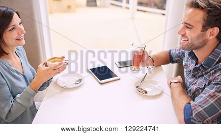 Old friends laughing and happy while they look at each other sitting in a beautiful light coffee shop with a smartphone and a tablet lying on the table infront of them.