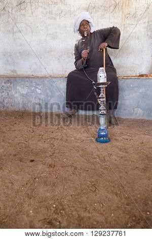 DARAW, EGYPT - FEBRUARY 6, 2016: Local camel salesman smoking shisha pipe.