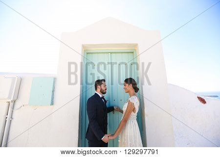 groom and bride holding hands near a green door vlue sky