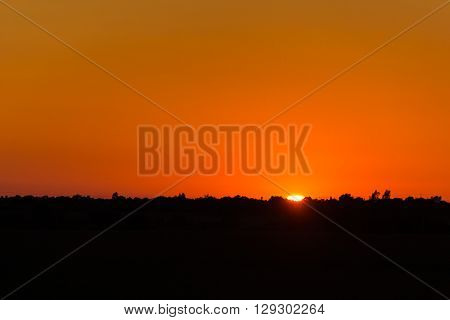 Horizontal photo with calm hot sunset on the background of horizontal silhouette forests and villages.