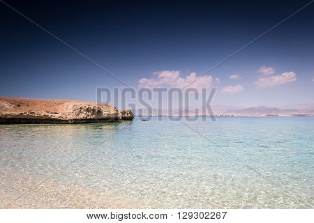 Horizontal photo with the sandy beach with calm clear sea deep blue sky and part of the island