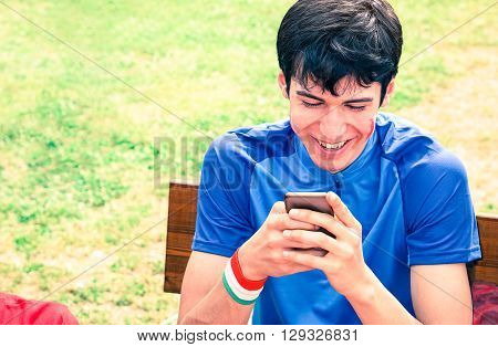 Joyful man watching mobile phone sitting on park bench - Smiling guy looking down to smartphone screen - Handsome young male portrait in sportswear busy with cellphone - Modern communication concept