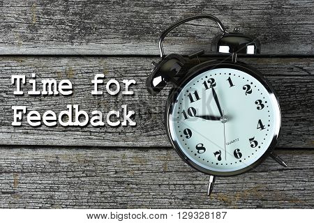 Black alarm clock on the rusty wooden table with word Time for Feedback